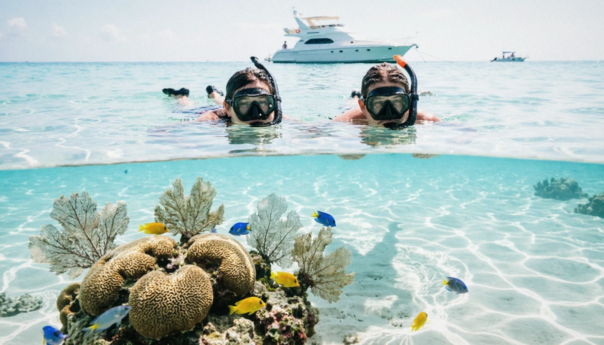Two snorkelers over a coral reef with a private yacht anchored behind them off Isla Mujeres on a Cancun yacht rental