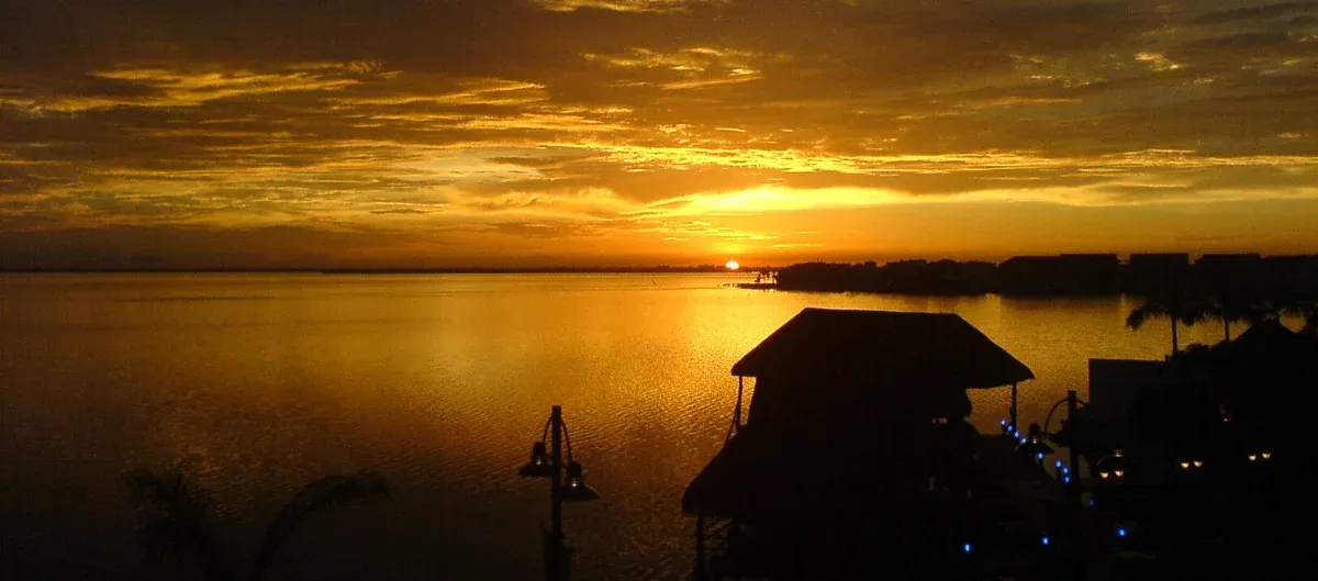 Golden sunset on Nichupte Lagoon with a palapa silhouette, the water of Cancun lagoon yacht cruises